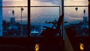 Vista da un balcone su una distesa d'acqua con una terraferma in lontananza, una sedia e una lampada.