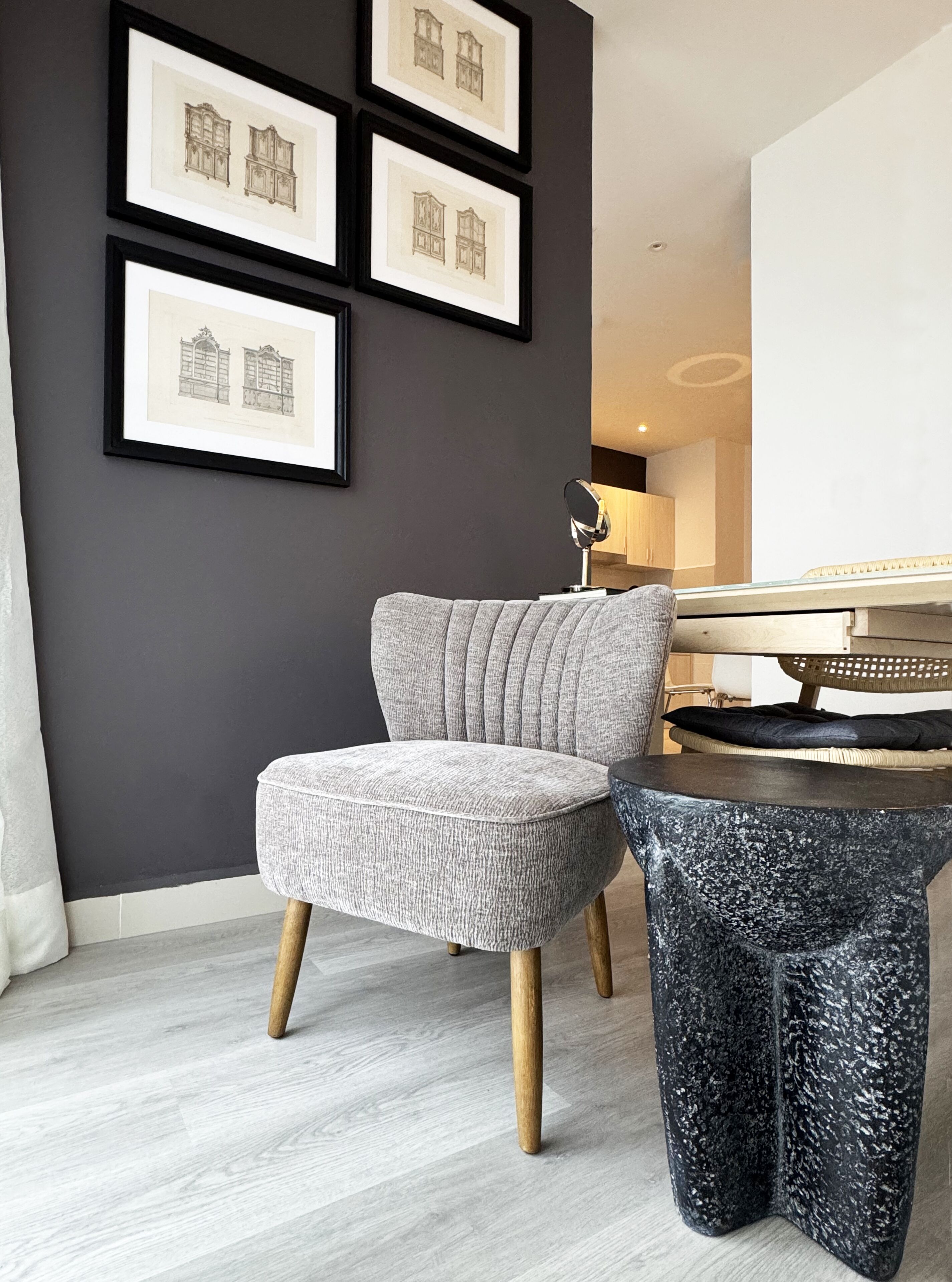A modern living room with a grey upholstered armchair, a small round side table, and framed architectural drawings on the wall.