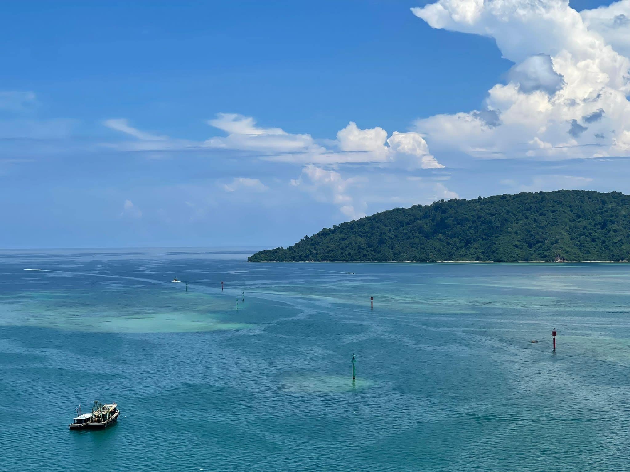 Un bateau sur des eaux turquoise et limpides, avec une île boisée qui se profile à l’horizon.