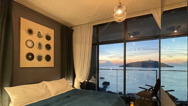 A bedroom with a large bed, a view of the sea, and a wall with circular decorations. - Seaview Bliss Studio - Tropical Elegance (Kota Kinabalu)