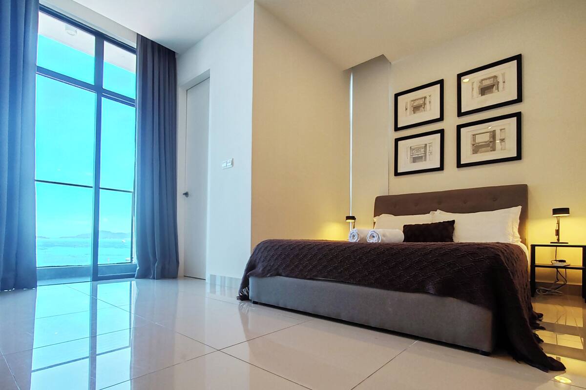 Een moderne slaapkamer met een groot bed, uitzicht naar buiten en ingelijste foto's aan de muur.