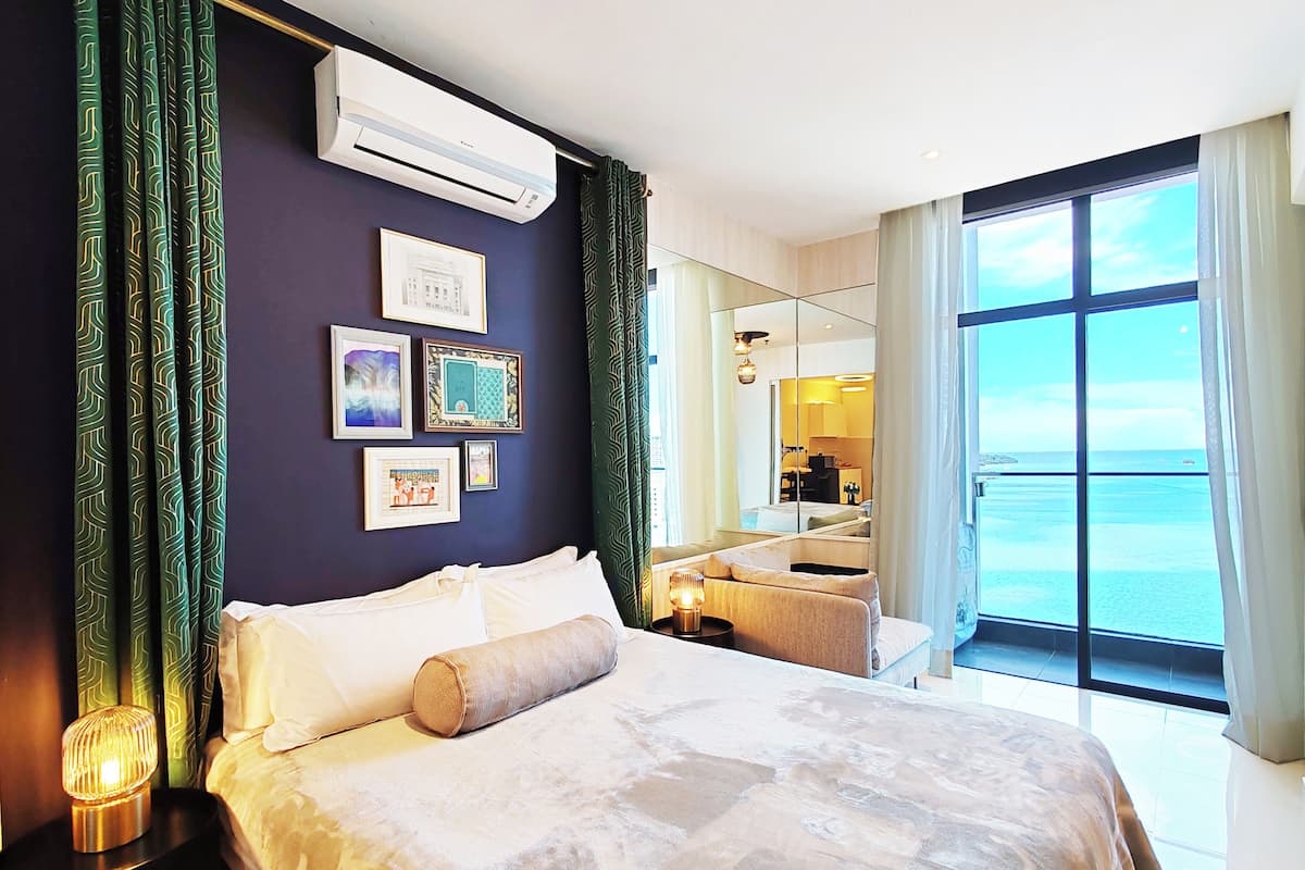 Een hotelkamer met een bed, een spiegel, uitzicht op zee en foto's in lijsten aan de muur.
