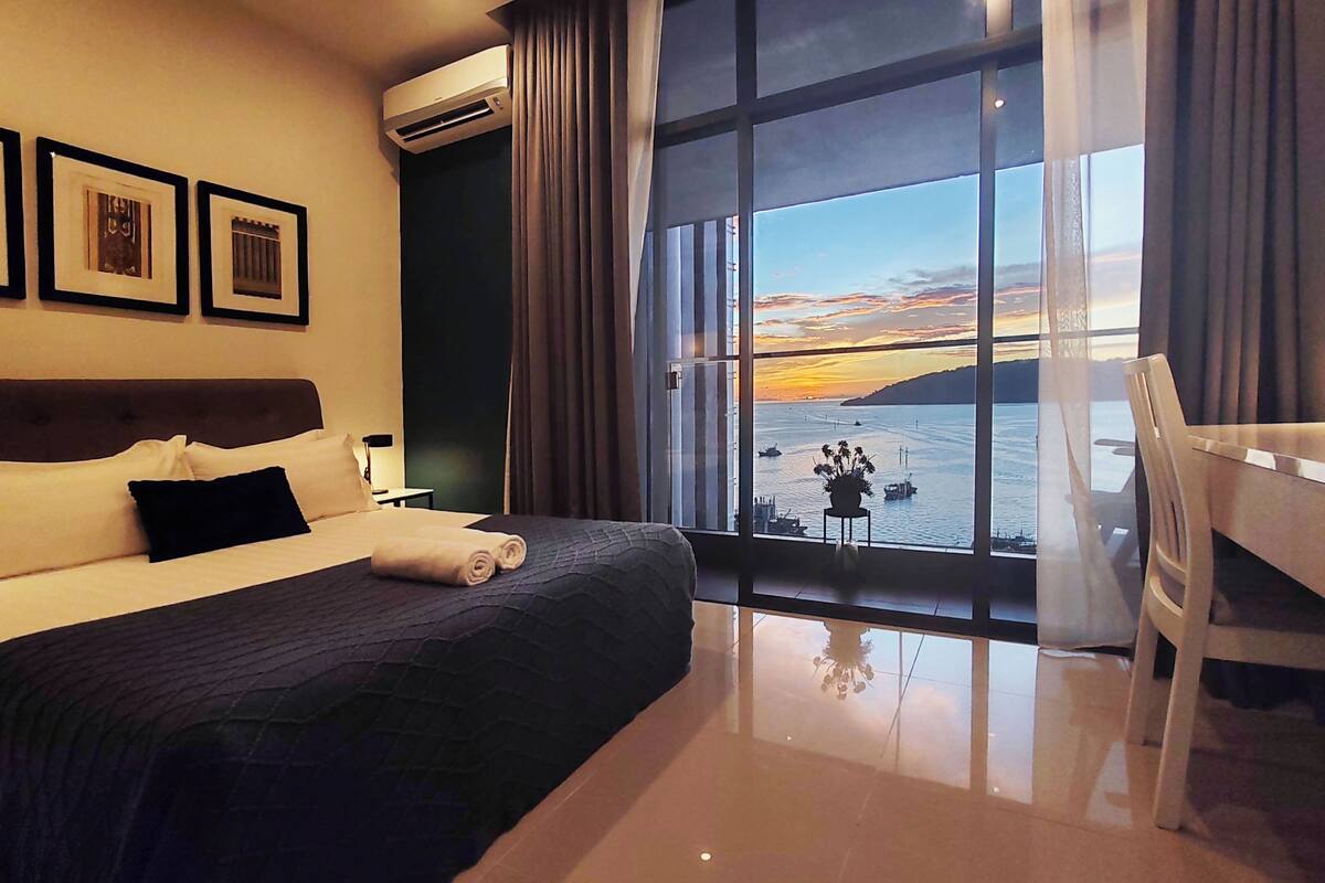 Een hotelkamer met een groot bed, een bureau en uitzicht op zee.