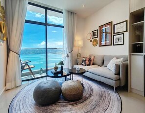 A living room with a large window, a sofa, a coffee table, and a rug. - Seaview Bliss Studio - Tropical Elegance (Kota Kinabalu)