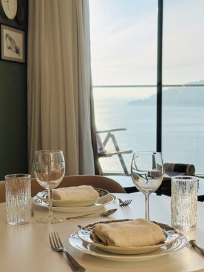 Une table dressée pour deux personnes, avec des verres à vin, des assiettes et des couverts, donnant sur une étendue d’eau.