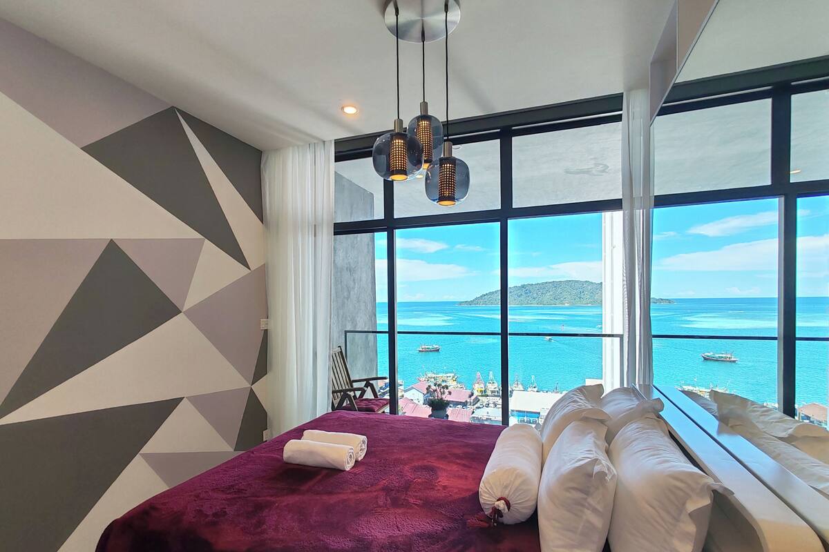 Een hotelkamer met een groot bed, uitzicht op zee en een geometrisch wandontwerp.