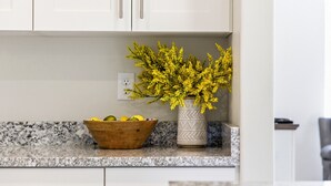 Eine Küche mit weißen Schränken, einer Arbeitsplatte aus Granit, einer Holtschale mit Zitronen und einer Vase mit gelben Blumen.