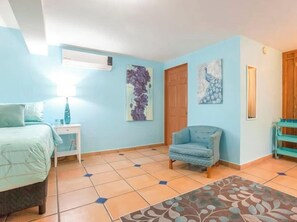 A bedroom with a bed, a chair, a nightstand, a wall-mounted air conditioner, and a door. - Private Suite Ideal for Solo Travelers Or Couples (La Paz)