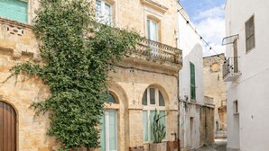 A narrow street with stone buildings, arched windows, and a large tree. - Dimora Alexanos by Symphonya Rentals (Alessano)