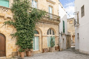 Una stretta via fiancheggiata da edifici in pietra, con finestre ad arco e un grande albero.