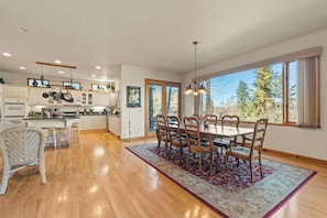 A spacious kitchen with white cabinets, a dining area with a table and chairs, and large windows offering a view of trees.