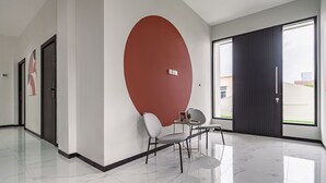 Un moderno vestíbulo de hotel con una gran pared roja, un área de descanso con una mesa y sillas, y un amplio ventanal con vistas al exterior.