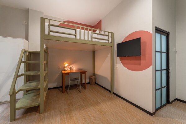 A bunk bed with a desk and chair, a small trash bin, and a TV mounted on the wall. - Cove Haven (Surabaya)