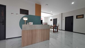 Zona de recepción de hotel con un mostrador, una barra de madera, una pared de acento color aguamarina, una lámpara de escritorio, un cuadro enmarcado, una planta pequeña y una puerta con el número 703.