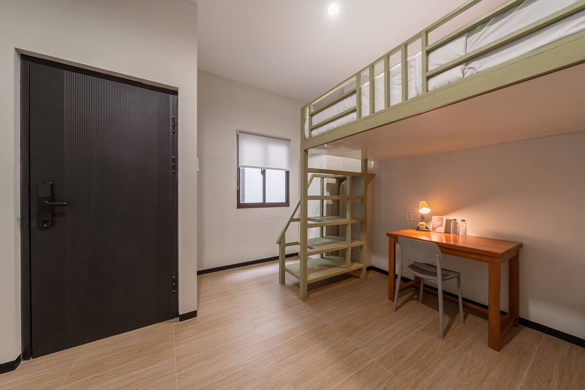 A room with a bunk bed, a desk with a chair, a window, and a door.
