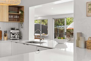 Eine moderne Küche mit weißen Schränken, einer Kaffeemaschine und einem großen Fenster mit Blick auf einen Garten.