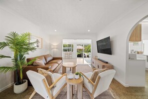 Een moderne woonkamer met een bank, stoelen, een salontafel, een televisie en een grote plant.