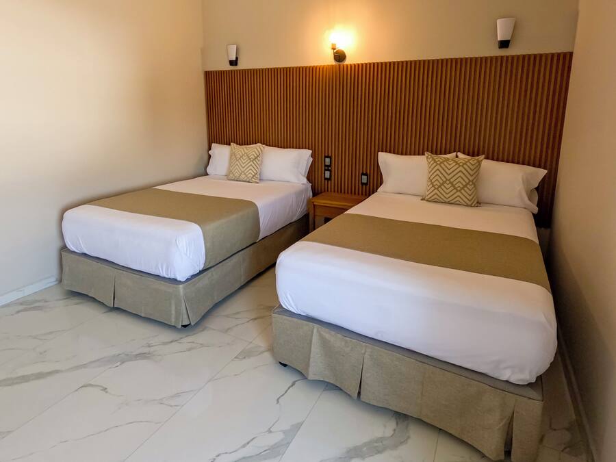 Two twin beds with beige bedding, a wooden headboard, and a wall-mounted light fixture.