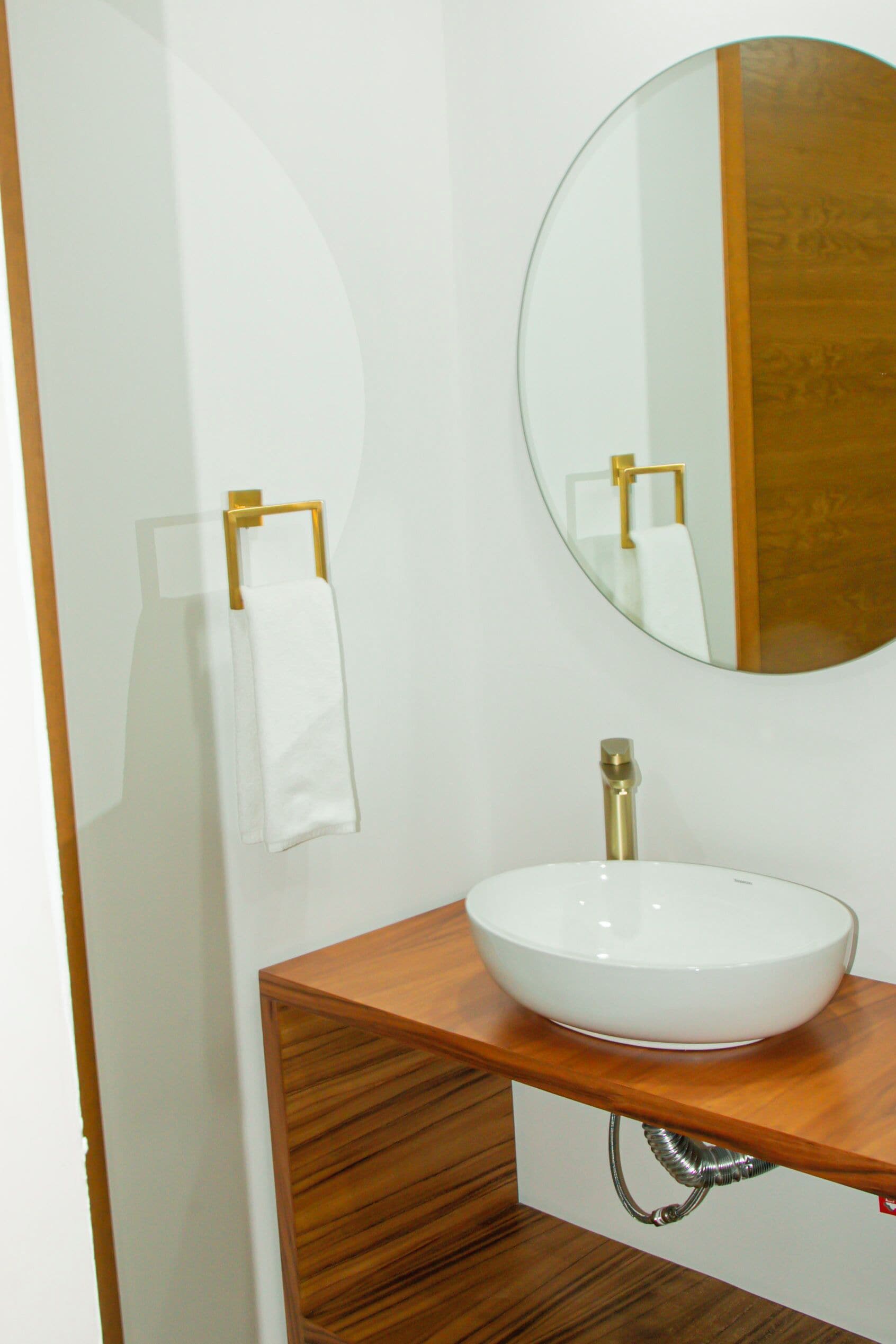 A bathroom with a white sink, a round mirror, and a towel rack.