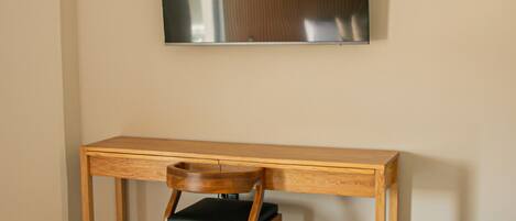 A wooden desk with a chair, a wall-mounted flat-screen TV, and a marble floor.