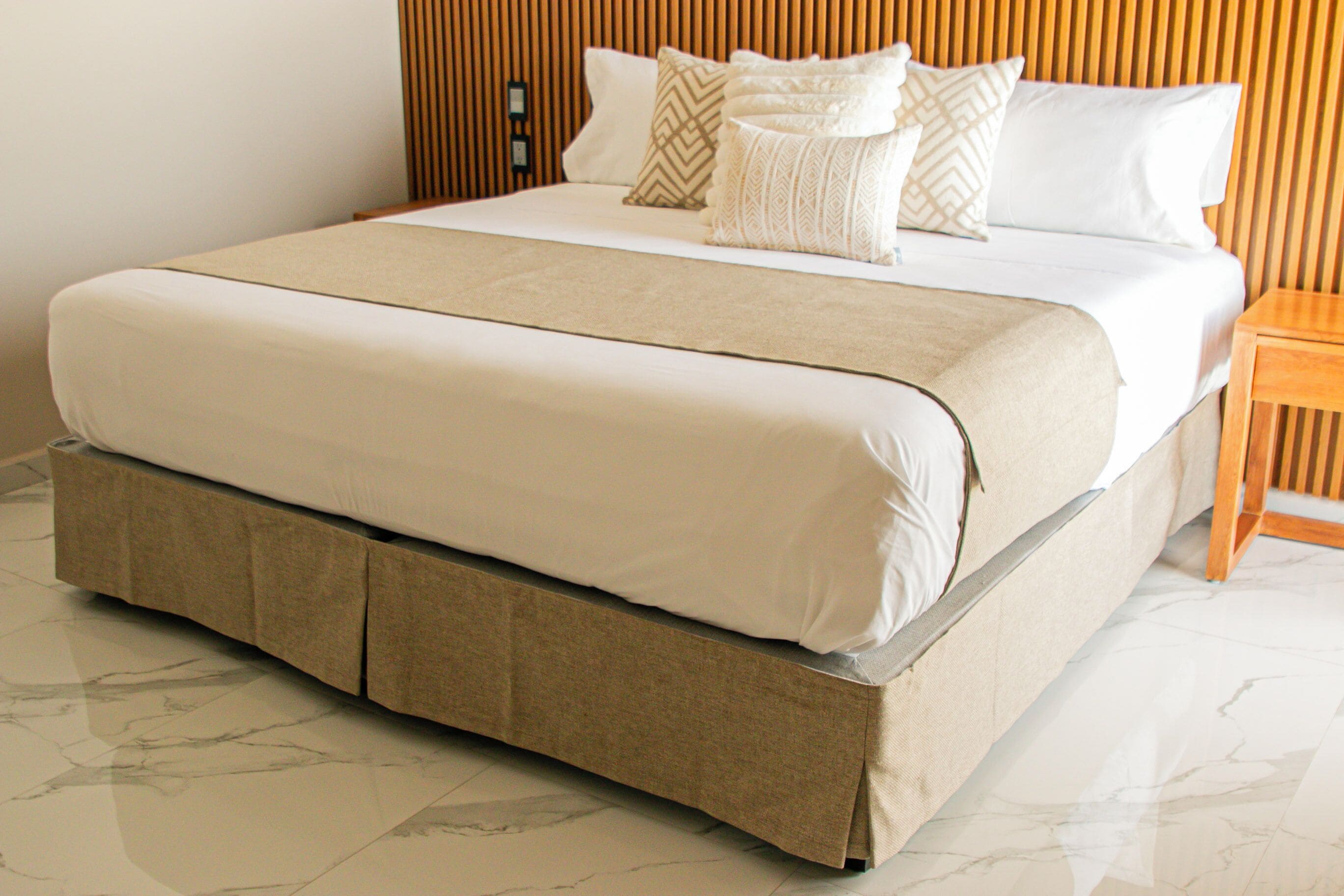 A bed with a wooden headboard, a beige bed skirt, and a white mattress.