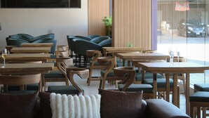 A modern cafe interior with wooden tables and chairs, a green sofa, and a view of the street through large windows. - Hotel JVD Inn - Tonalá Centro (Tonalá)