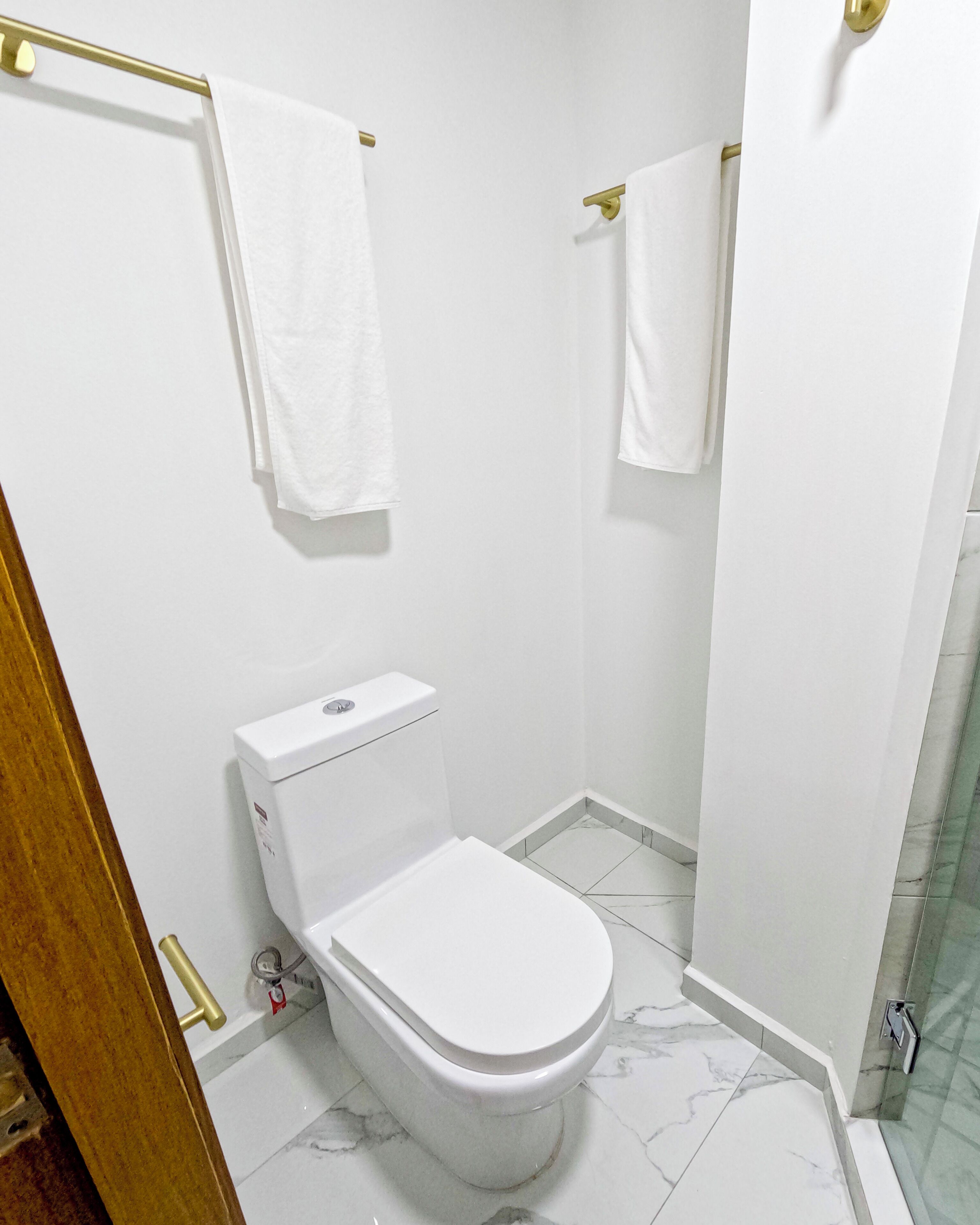 A small, white bathroom with a toilet, a shower, and a towel rack.