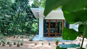 Un bâtiment doté d’une grande porte vitrée, entouré de plantes en pot et d’arbres.