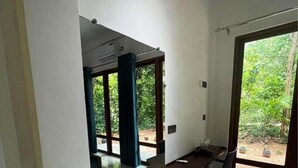 Une chambre moderne équipée d’un bureau, de deux poufs verts, d’une chaise et d’une grande fenêtre donnant sur un paysage verdoyant.