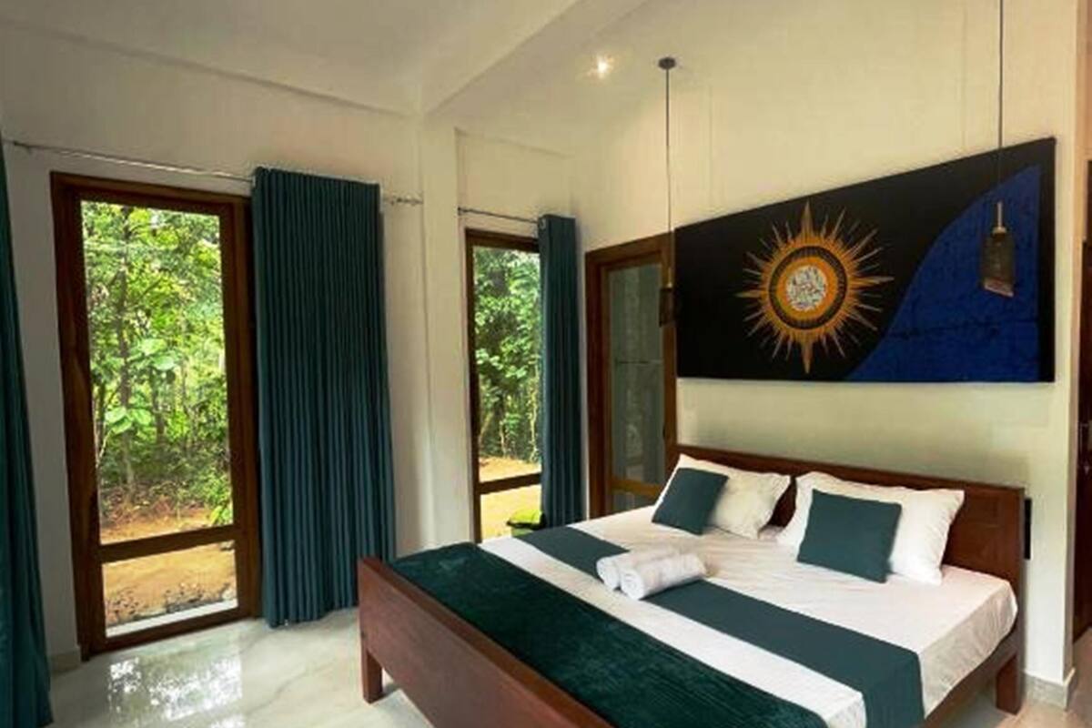 Une chambre à coucher moderne, avec un grand lit, une vue sur la verdure par les fenêtres et un tableau accroché au mur.