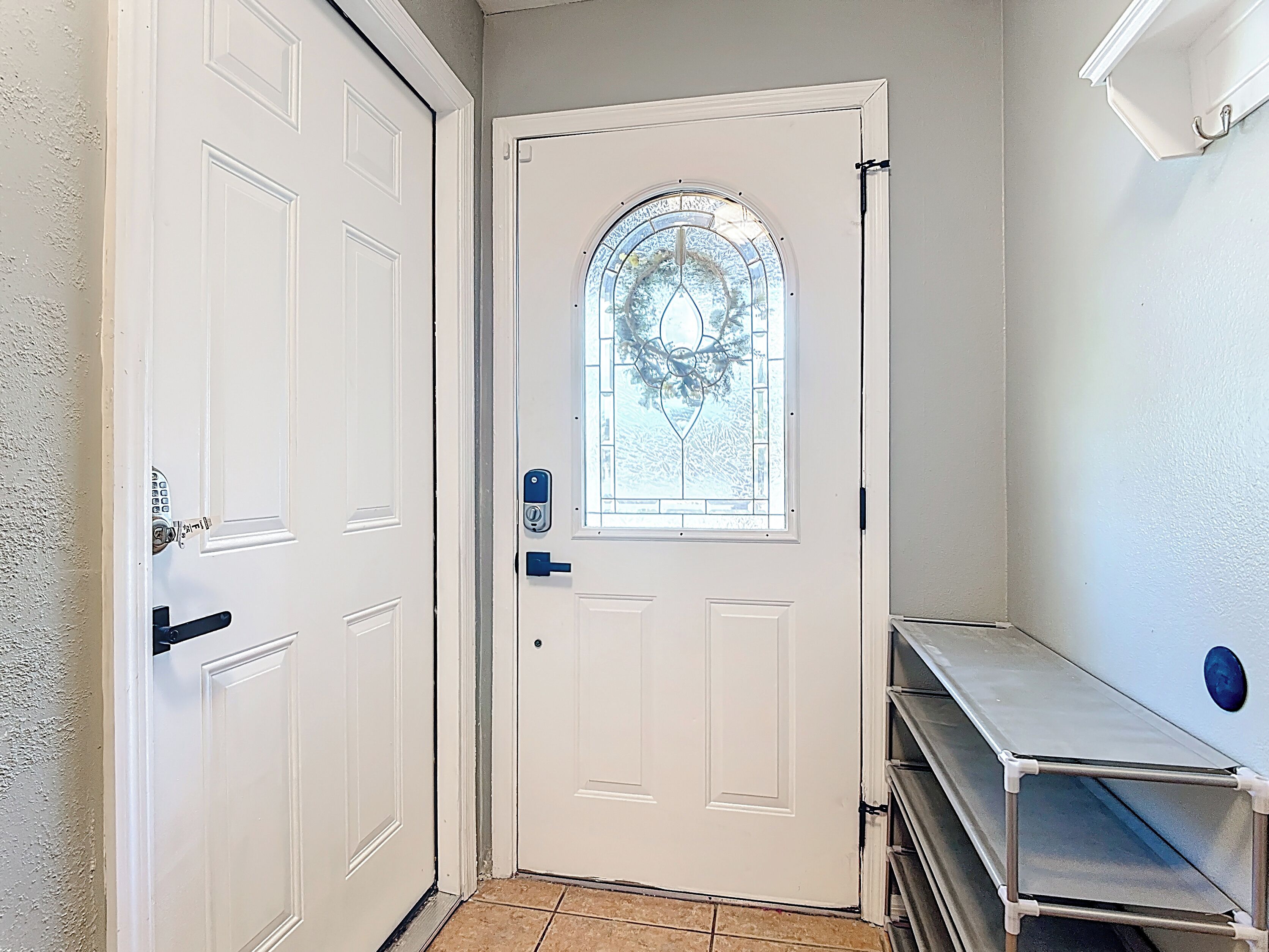 A white door with a glass window, a doorbell, and a metal shelf to the right.