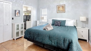 Une chambre à coucher comprenant un lit, une table de chevet, une lampe, une commode, un miroir et un tableau accroché au mur.