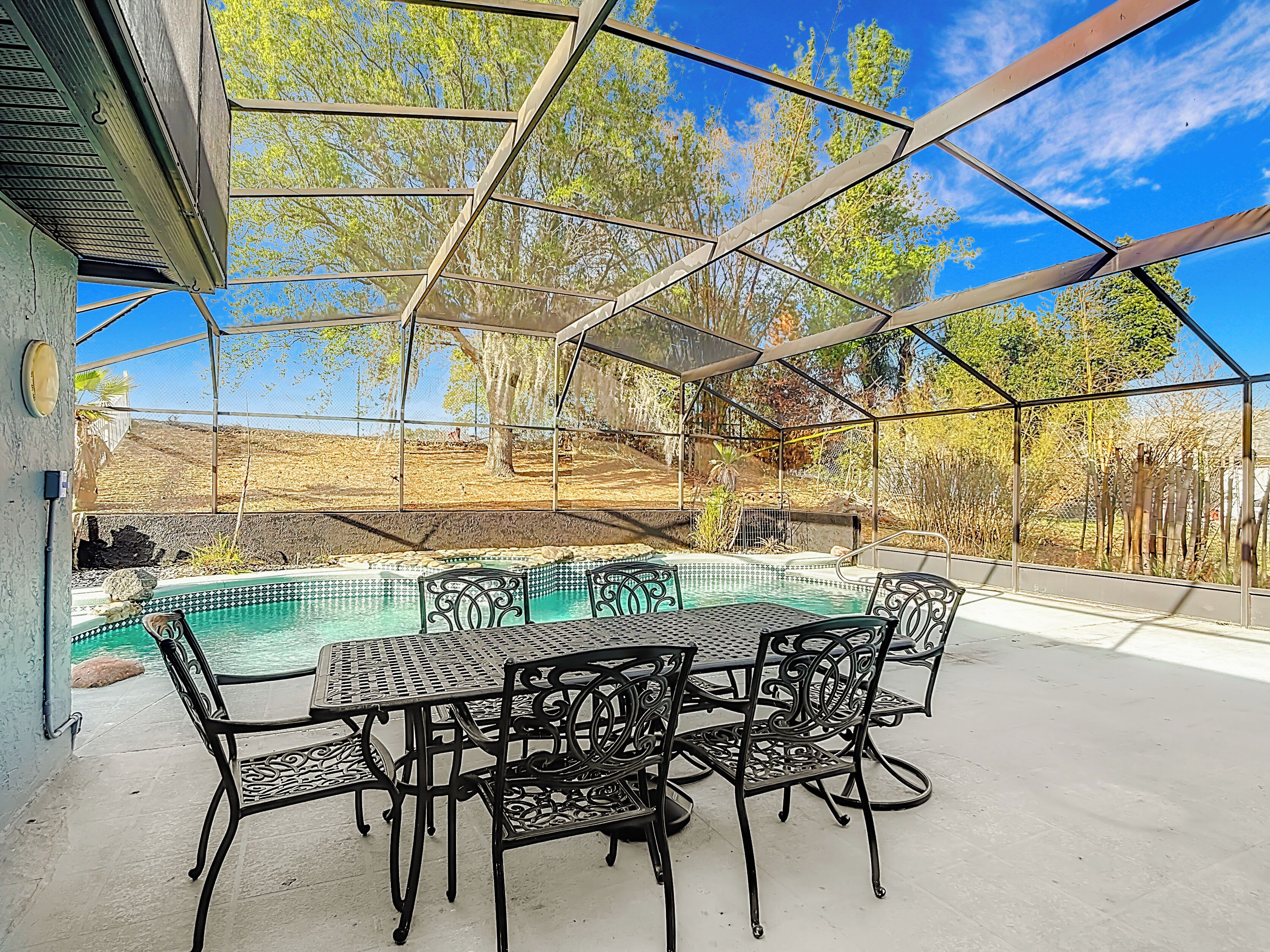 A covered outdoor area with a pool, metal chairs, and a table.