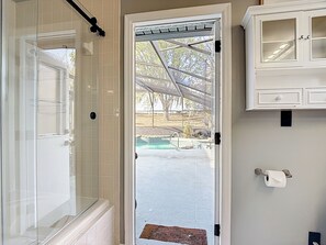 Un baño con cabina de ducha de vidrio, pared de azulejos blancos, un mueble blanco con puertas de cristal y vistas a una piscina exterior.