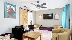 Un salon avec un canapé, une table en bois, un ventilateur de plafond, un téléviseur et une porte.