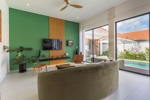 Ein modernes Wohnzimmer mit grüner Akzentwand, einem Flachbildfernseher, einem großen Sofa und Blick auf einen Pool im Freien.