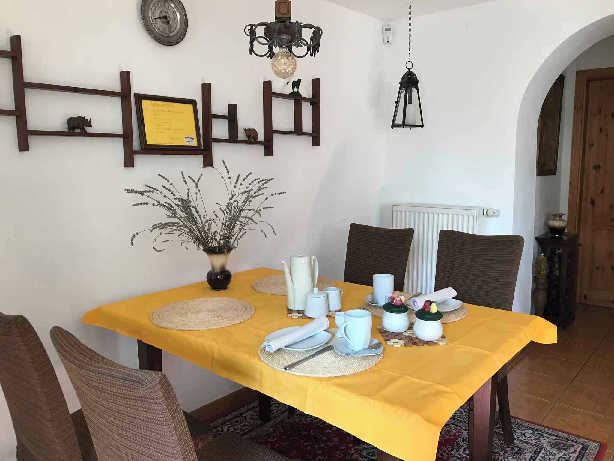 A dining table with yellow tablecloth, white plates, and a vase with dried flowers.