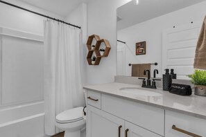 A modern bathroom with a toilet, shower curtain, vanity with a sink, mirror, and towel rack.