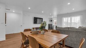 Una sala de estar moderna con una mesa de comedor de madera, un sofá gris y un televisor montado en la pared.