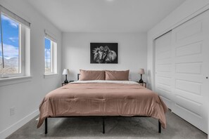 A bedroom with a bed, two bedside tables, a wall-mounted artwork, and a large window.