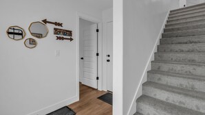 Una escalera conduce a una plataforma con una puerta blanca, una pared con espejos decorativos y un letrero, y un piso de madera.