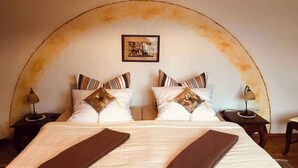 Uma cama com duas almofadas, uma mesa de cabeceira com abajur e um quadro pendurado na parede.