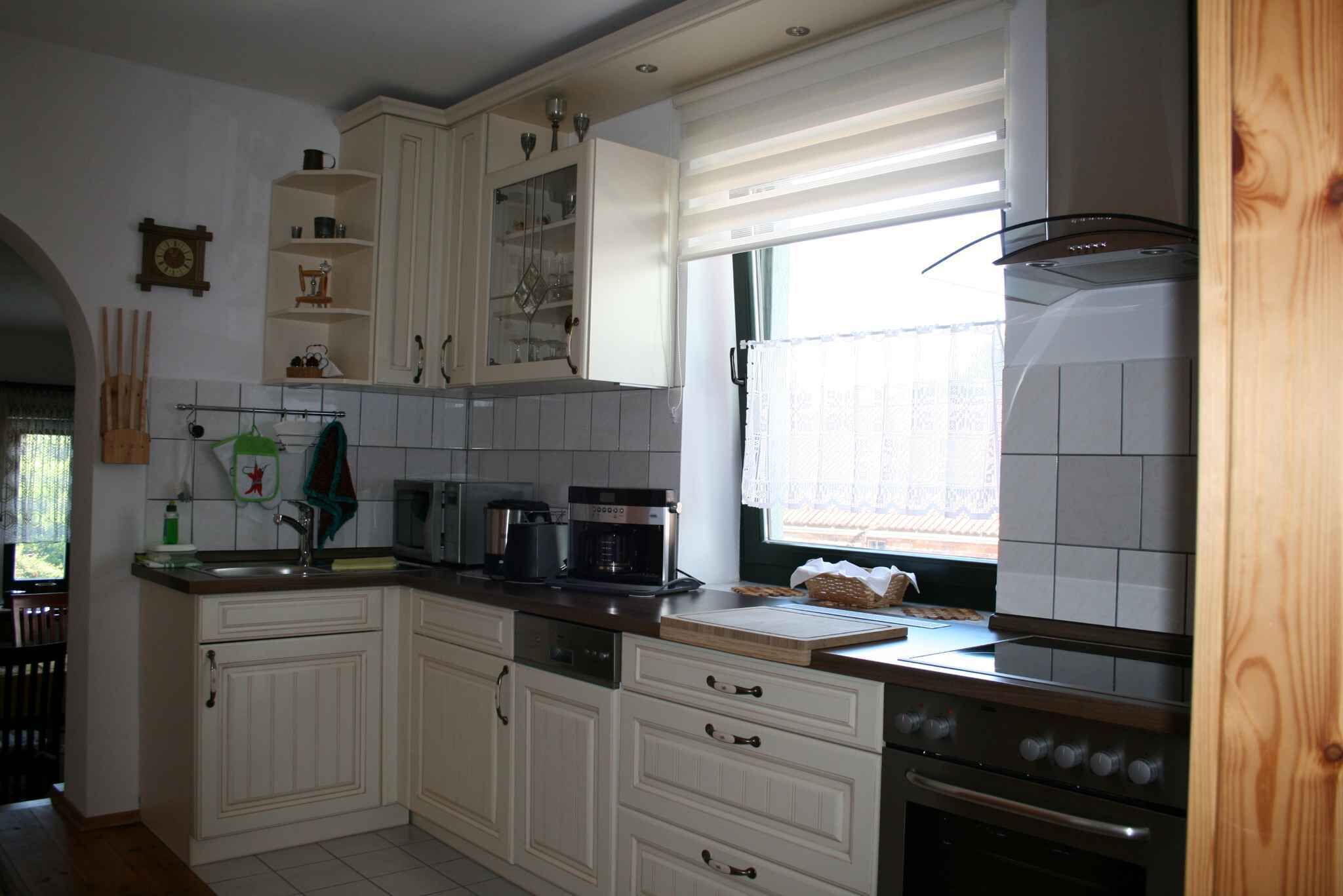 A kitchen with white cabinets, a stove, a coffee maker, and a window with blinds.