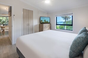 A bedroom with a large bed, a desk, and a window with a view. - Oasis 12 & Free Buggy - Hamilton Island (Hamilton Island)
