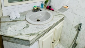 Une salle de bain avec un lavabo en marbre, un miroir, une douche et un porte-serviettes.