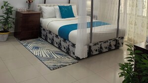 Une chambre à coucher avec un lit à baldaquin, un ventilateur de plafond, une table de chevet ornée d’un vase et un tapis à motifs.