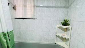 Une salle de bain avec une baignoire, un rideau de douche, une serviette et une étagère sur laquelle est posée une plante.