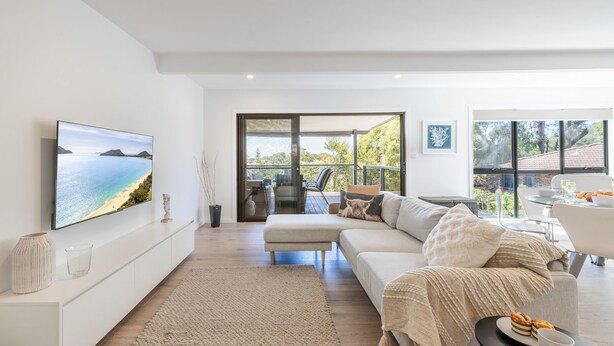 Una sala moderna con un televisor de pantalla plana grande, un sofá, un comedor y un balcón con mobiliario exterior.