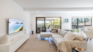 Ein modernes Wohnzimmer mit großem Flachbildfernseher, einer Couch, einem Essbereich und einem Balkon mit Gartenmöbeln.
