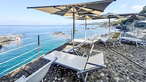 Ein Strandloungebereich mit Liegestühlen und Sonnenschirmen mit Blick auf das Meer und die felsige Küste.